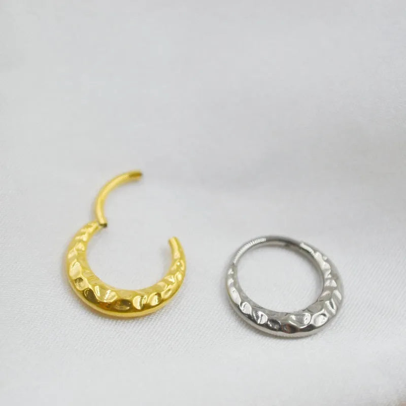 Close-up of a titanium concave-convex nose ring in gold, showing its carved texture and circular shape.