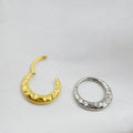 Close-up of a titanium concave-convex nose ring in gold, showing its carved texture and circular shape.