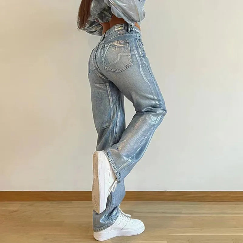 Women's washed blue high-waist straight-leg jeans with silver contrast hardware on a denim background.
