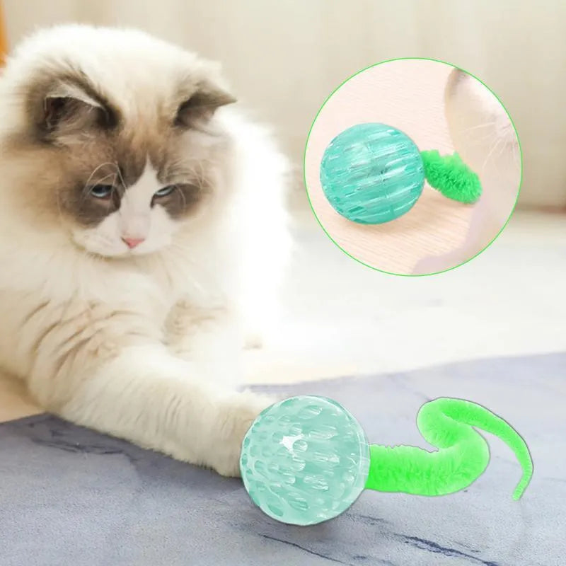 Green bouncy ball cat toy with plush tail on wooden floor