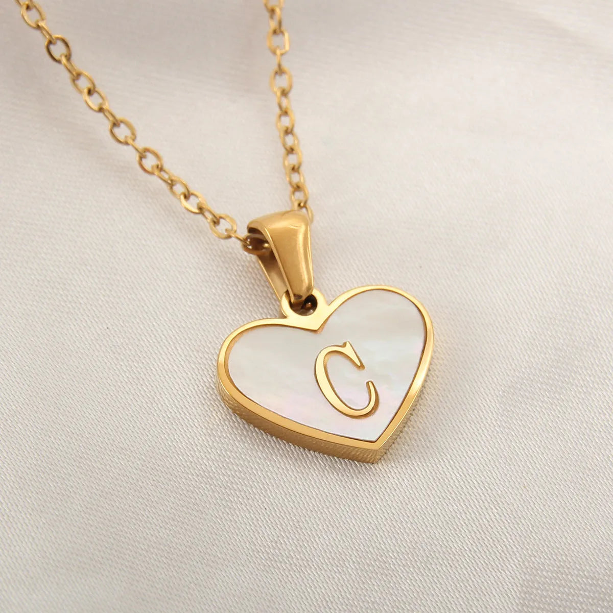 Gold-plated heart necklace with white shell pendant showing initial engraving on stainless steel chain