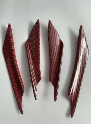 Set of four carbon fibre pattern bumper blade spoilers for car modification on a black background.