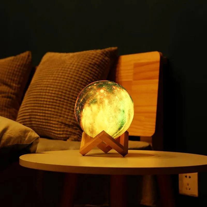 3D printed spherical lunar surface night light glowing with soft yellow and white LED light on a table.