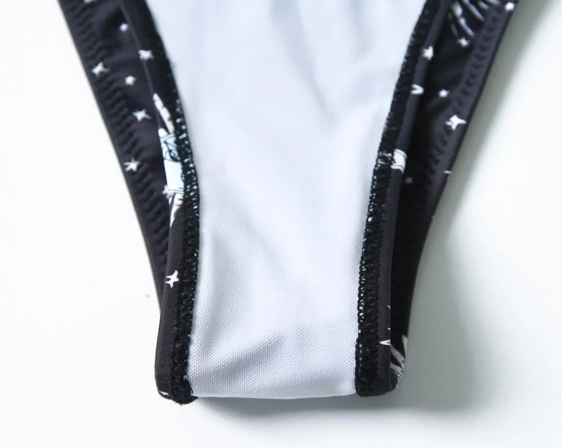 Black one-piece swimsuit with a bikini print pattern, showing backless design.