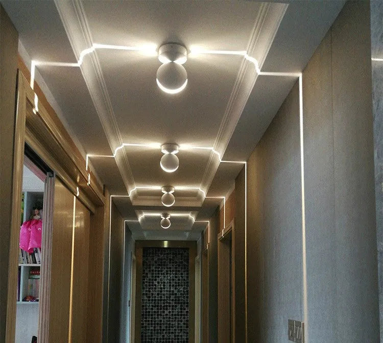 Modern aluminium LED bar wall lamp with glass lens, shown in a corridor setting.