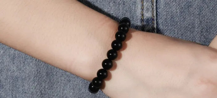 Black agate bracelet with geometric 8mm beads on a black elastic cord, laid flat.