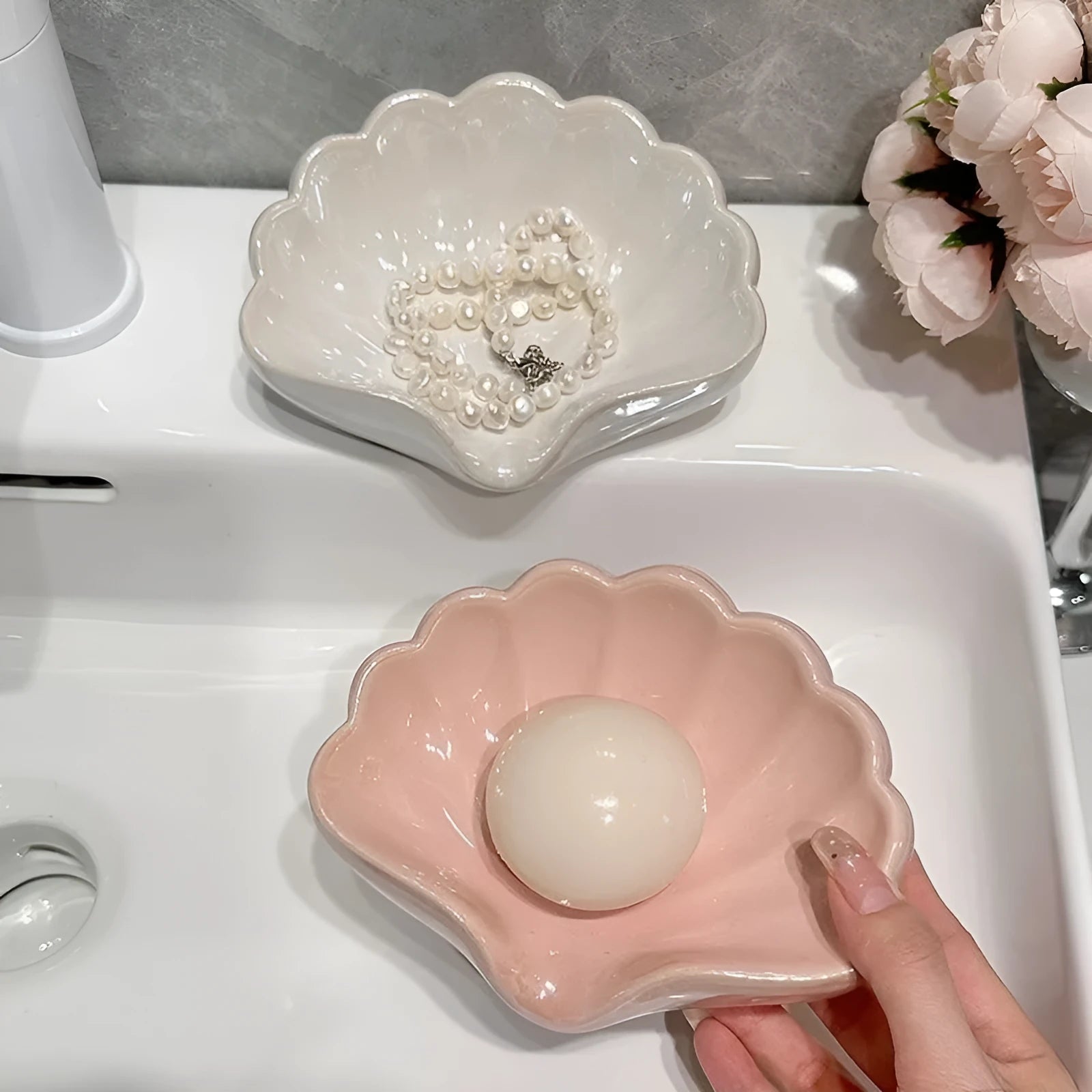 White or pink plastic shell-shaped soap dish with raised design on a bathroom counter.