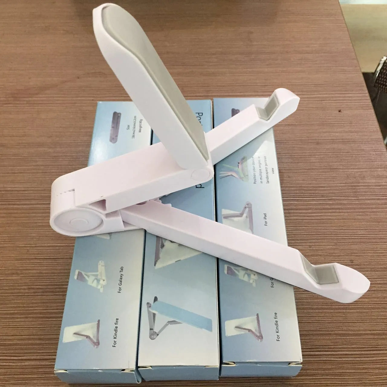 Black foldable tablet holder standing upright with a tablet in landscape mode on a wooden desk