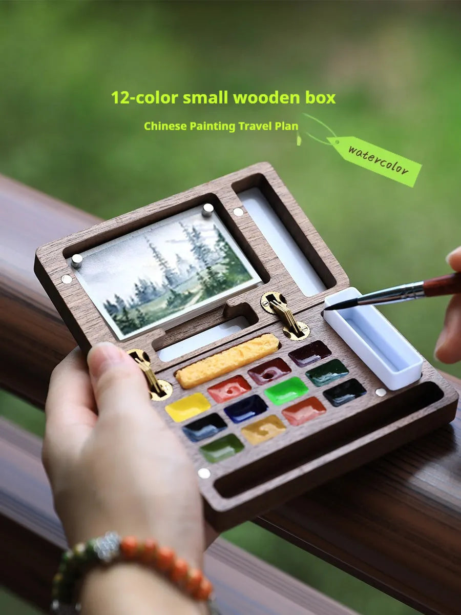 Mini walnut wooden box open to show watercolour paint pans in a portable artist travel set.