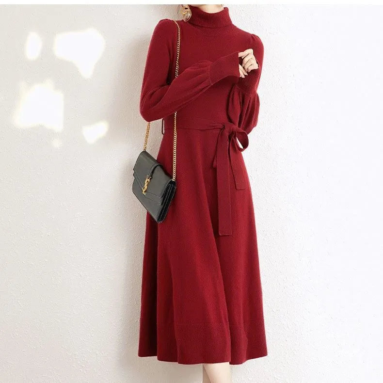 A woman wearing a rose red turtleneck knit dress with long sleeves, an elastic waist, and a loose mid-length hem.