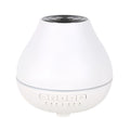 Round white Bluetooth humidifier and essential oil diffuser with night light on a wooden surface.