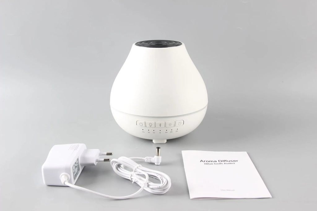 Round white Bluetooth humidifier and essential oil diffuser with night light on a wooden surface.