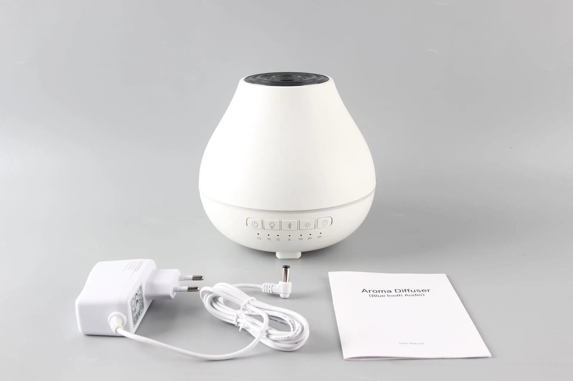 Round white Bluetooth humidifier and essential oil diffuser with night light on a wooden surface.