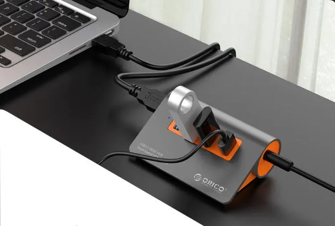 Dark grey and orange aluminium USB C hub with four USB 3.1 ports and a long black data cable.