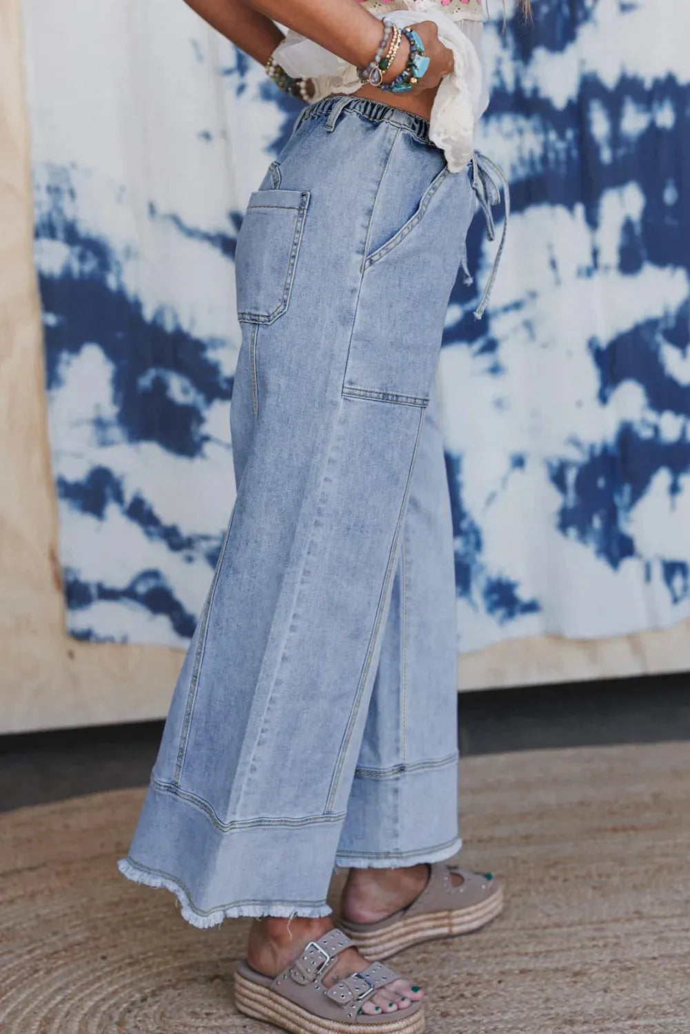 Beau blue wide-leg women's denim trousers with an elasticated drawstring waist and raw hem seam detail laid flat.