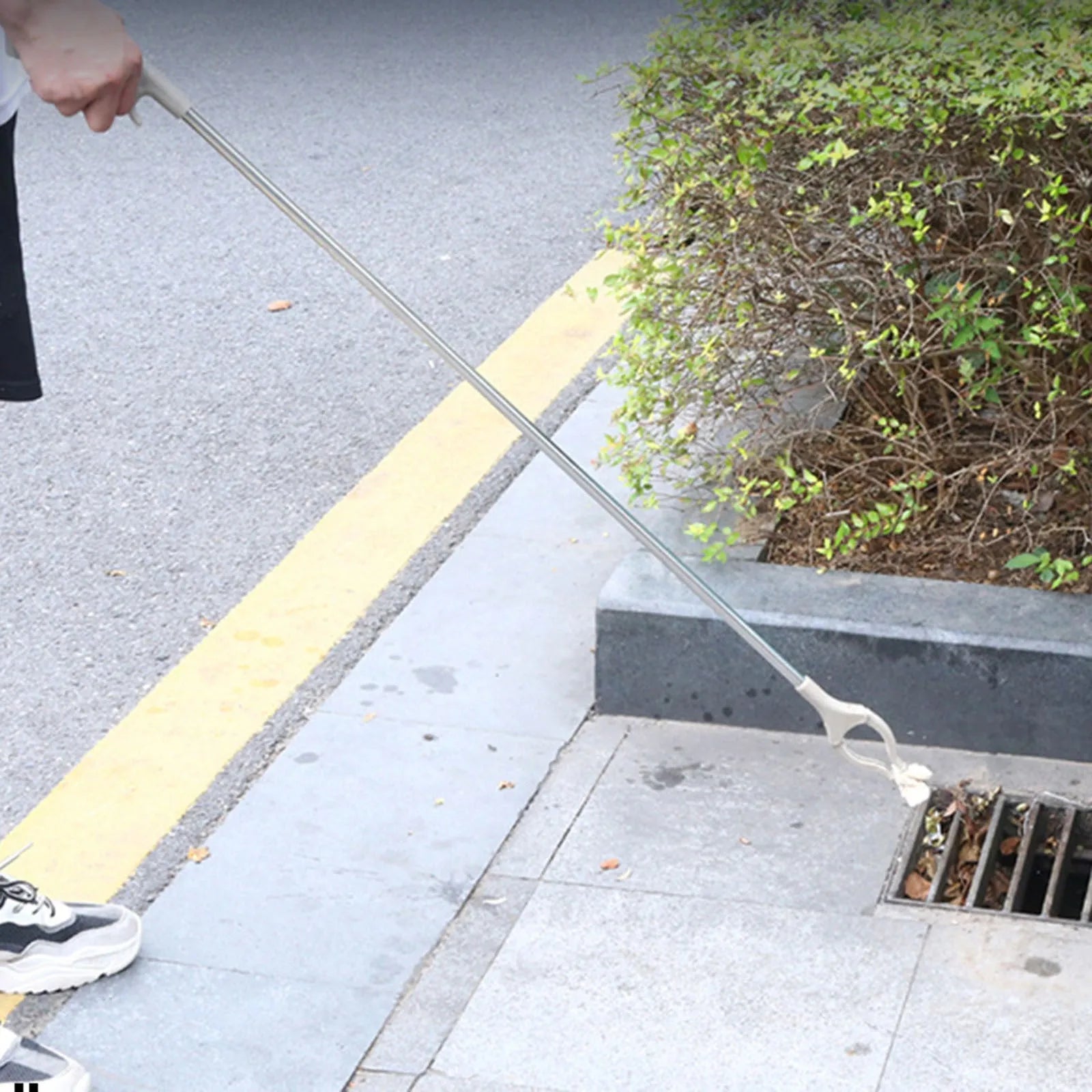 Long-handled stainless steel garbage picker pliers with a push-type handle.