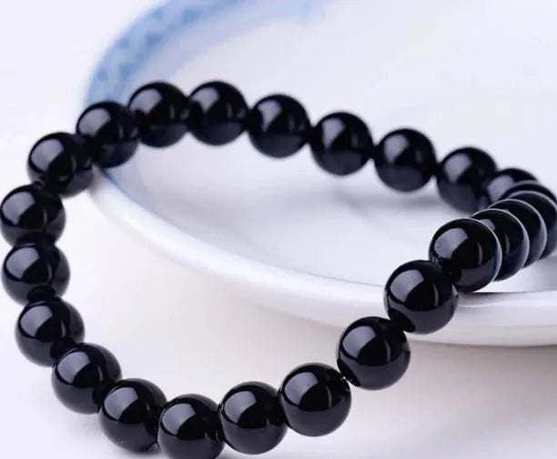 Black agate bracelet with geometric 8mm beads on a black elastic cord, laid flat.
