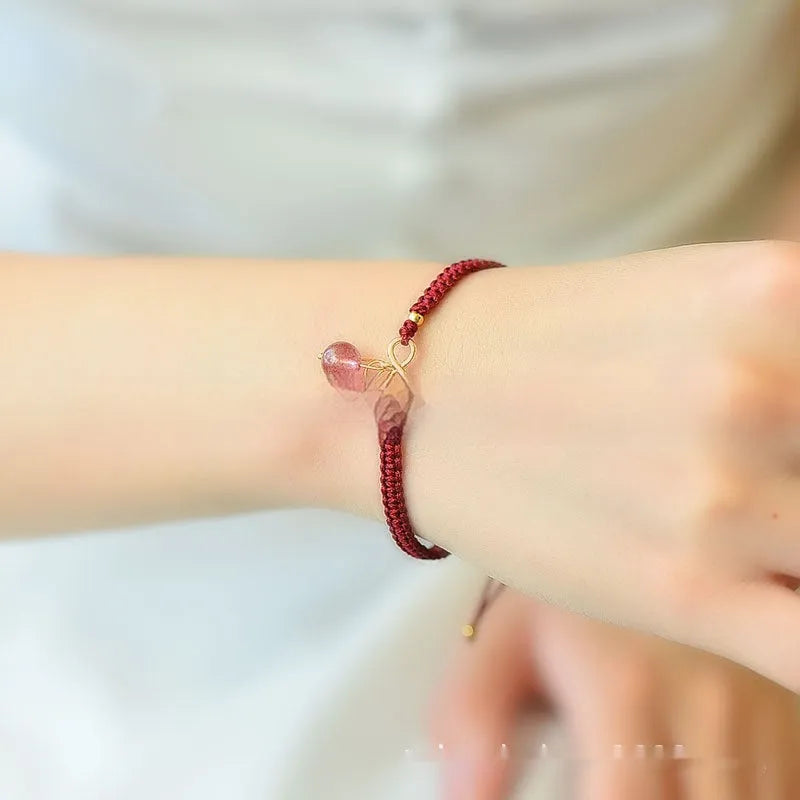Close-up of a women's natural crystal bracelet with a detailed cherry charm in strawberry quartz colour.
