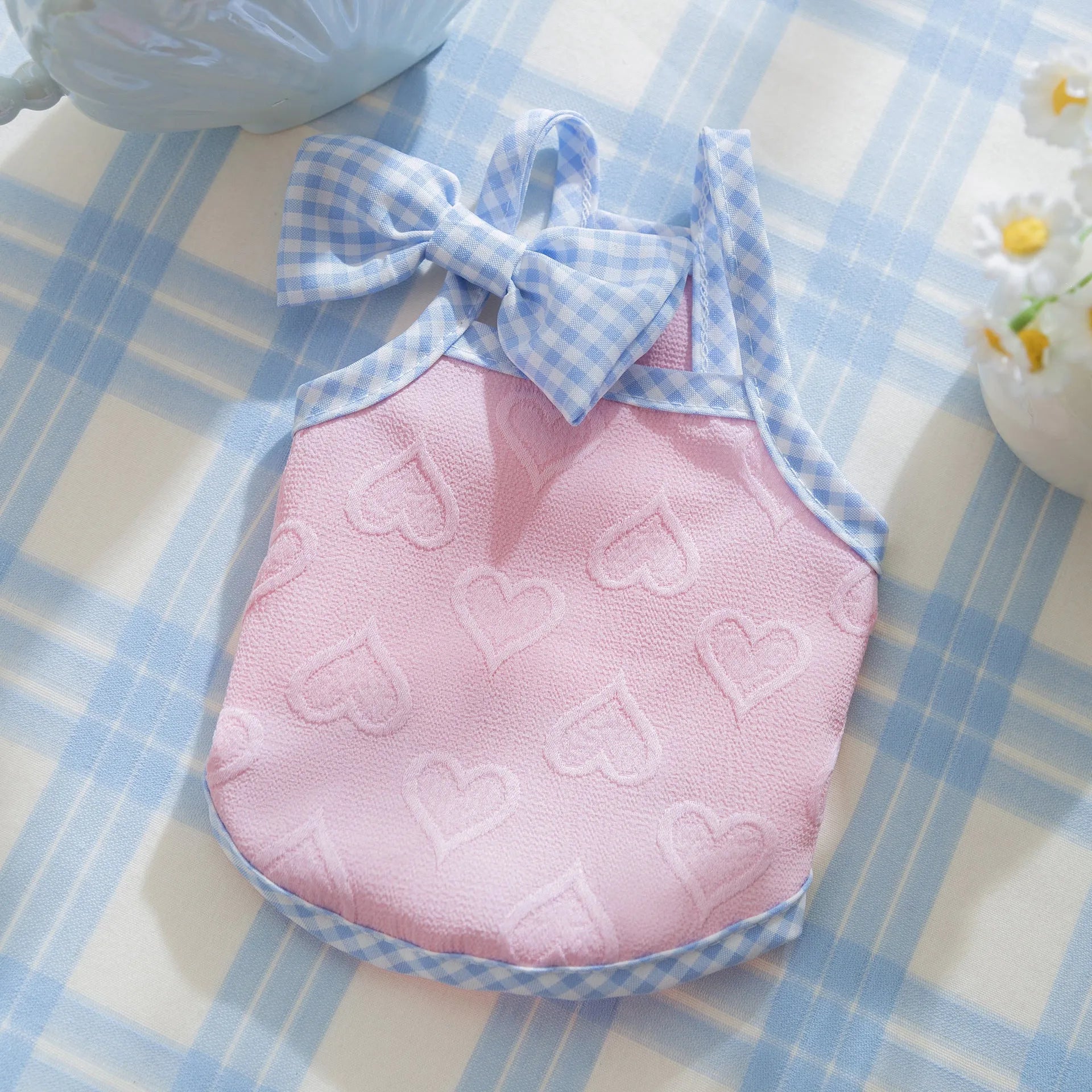 Small dog wearing a blue heart-texture vest with bow suspenders and a matching hairband.