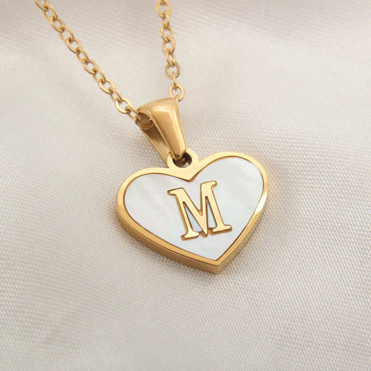 Gold-plated heart necklace with white shell pendant showing initial engraving on stainless steel chain