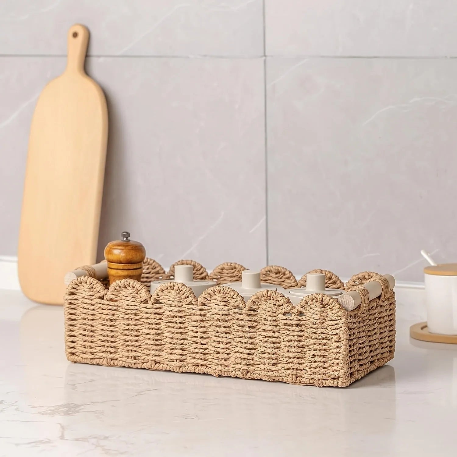 A minimalist woven paper storage basket in khaki colour on a wooden table, holding remote controls and pens.