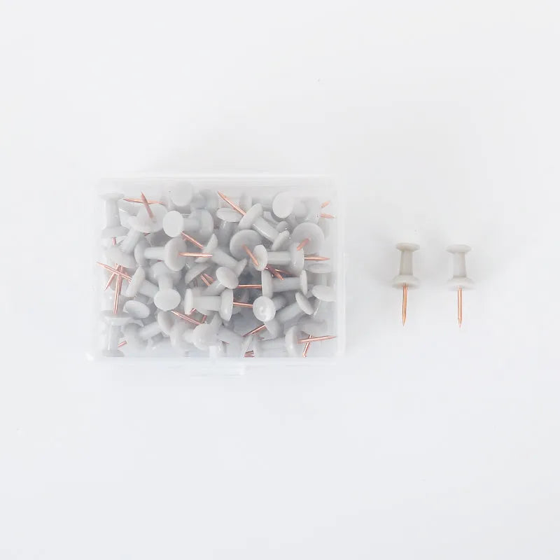 Morandi colour push pins in green, grey, and pink with three different head designs on cork board