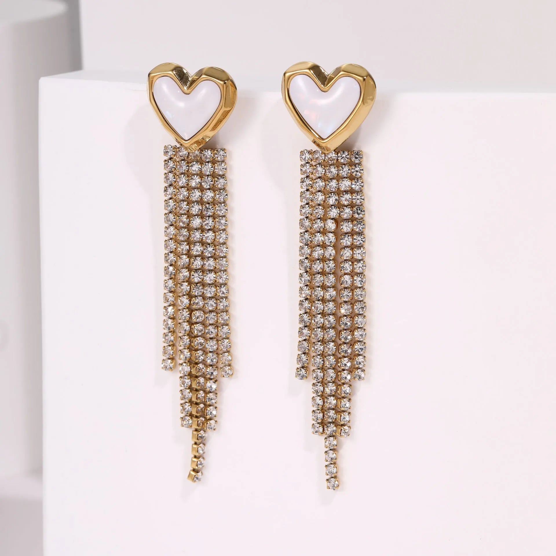 Close-up of a women's stainless steel earring with a heart shape and a dangling geometric tassel featuring diamond and star details.