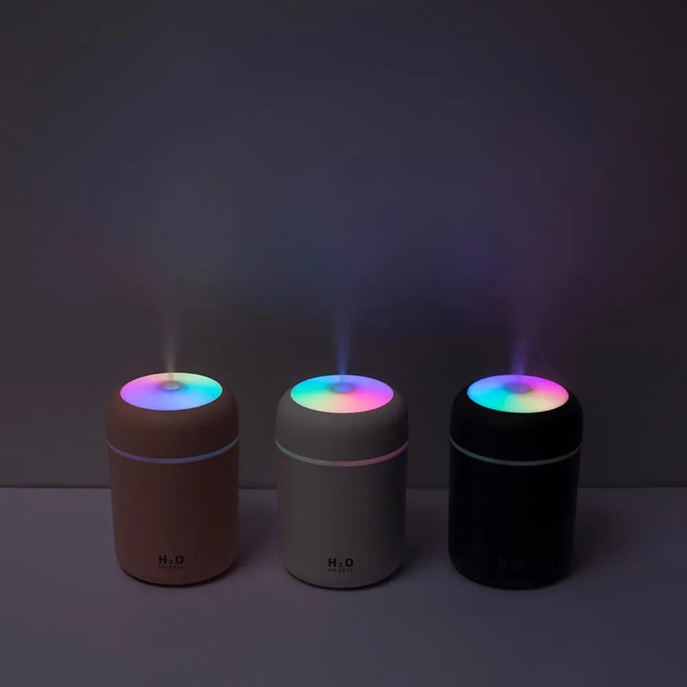 Pink USB mini humidifier with LED lights on wooden desk beside laptop