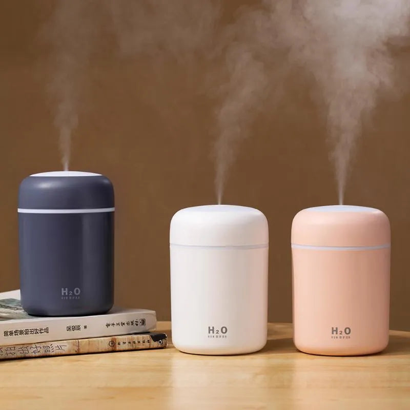 Pink USB mini humidifier with LED lights on wooden desk beside laptop