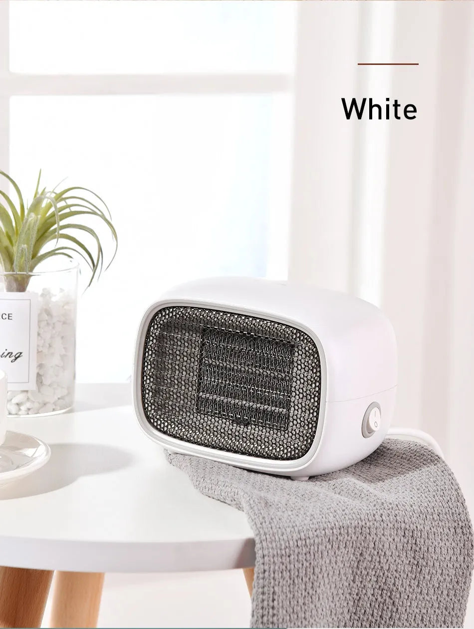 Compact green mini ceramic desk heater with metal mesh front grille, shown next to a pen for scale.