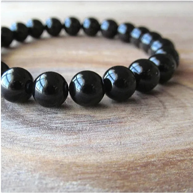 Black agate bracelet with geometric 8mm beads on a black elastic cord, laid flat.