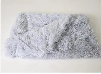 Soft grey long plush pet blanket for dogs on a wooden floor next to a kennel.