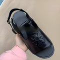 Men's black embroidered floral beach sandals with flat heel on a sandy background.