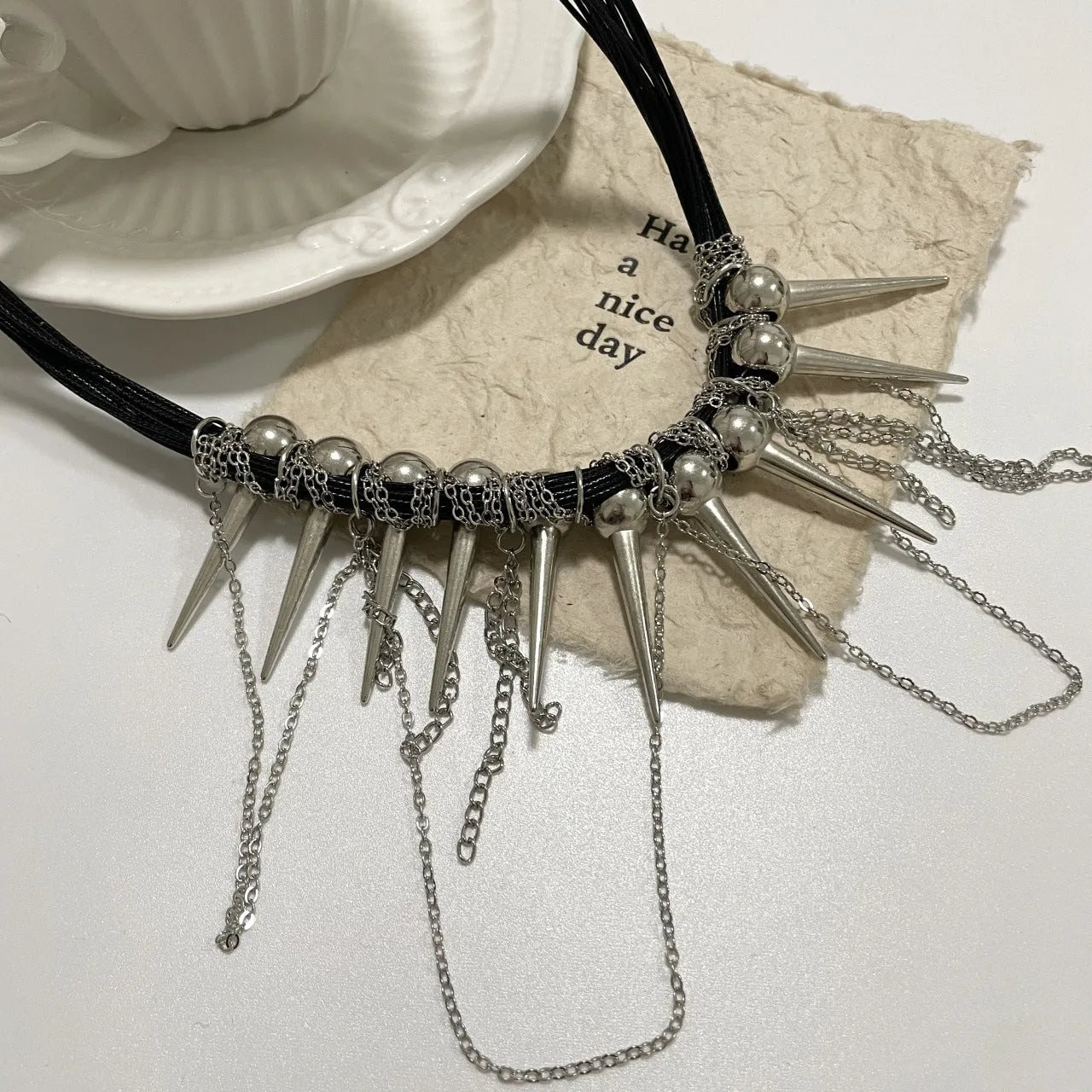 Leather necklace with winding round beads, rivet details, and a long tassel pendant in a metallic colour.