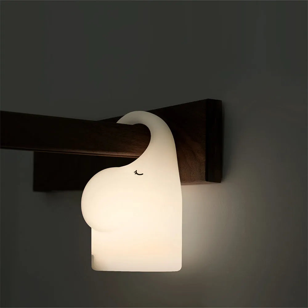 DOMI elephant-shaped silicone night light with warm white glow on a bedside table.