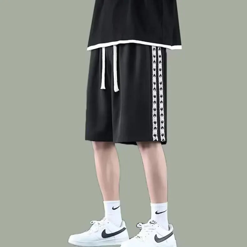 Men's black loose-fit polyester track pants with an elasticated waist, shown in a casual setting.
