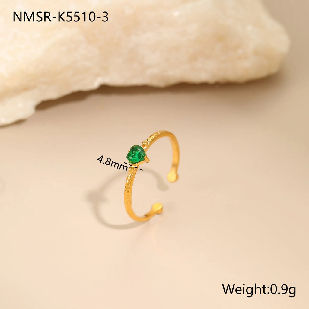 Open-ended geometric stainless steel ring with a green zircon heart inlay on a grey background.