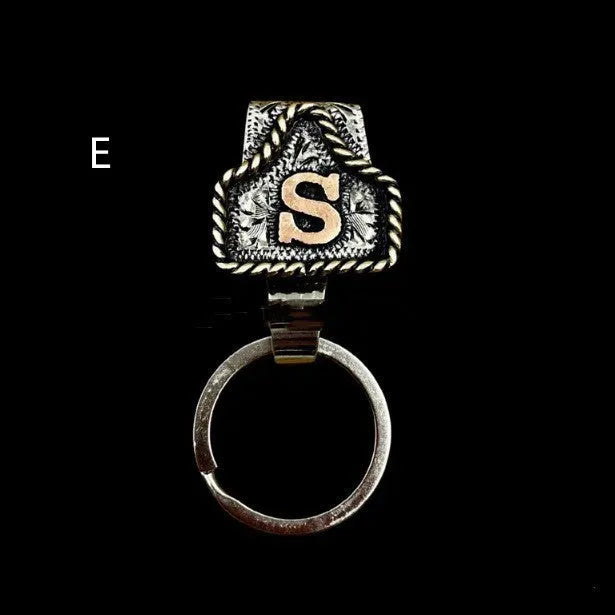 Handmade metal cow tag belt keychain showing one of 26 colour options, each marked with a different alphabet letter.
