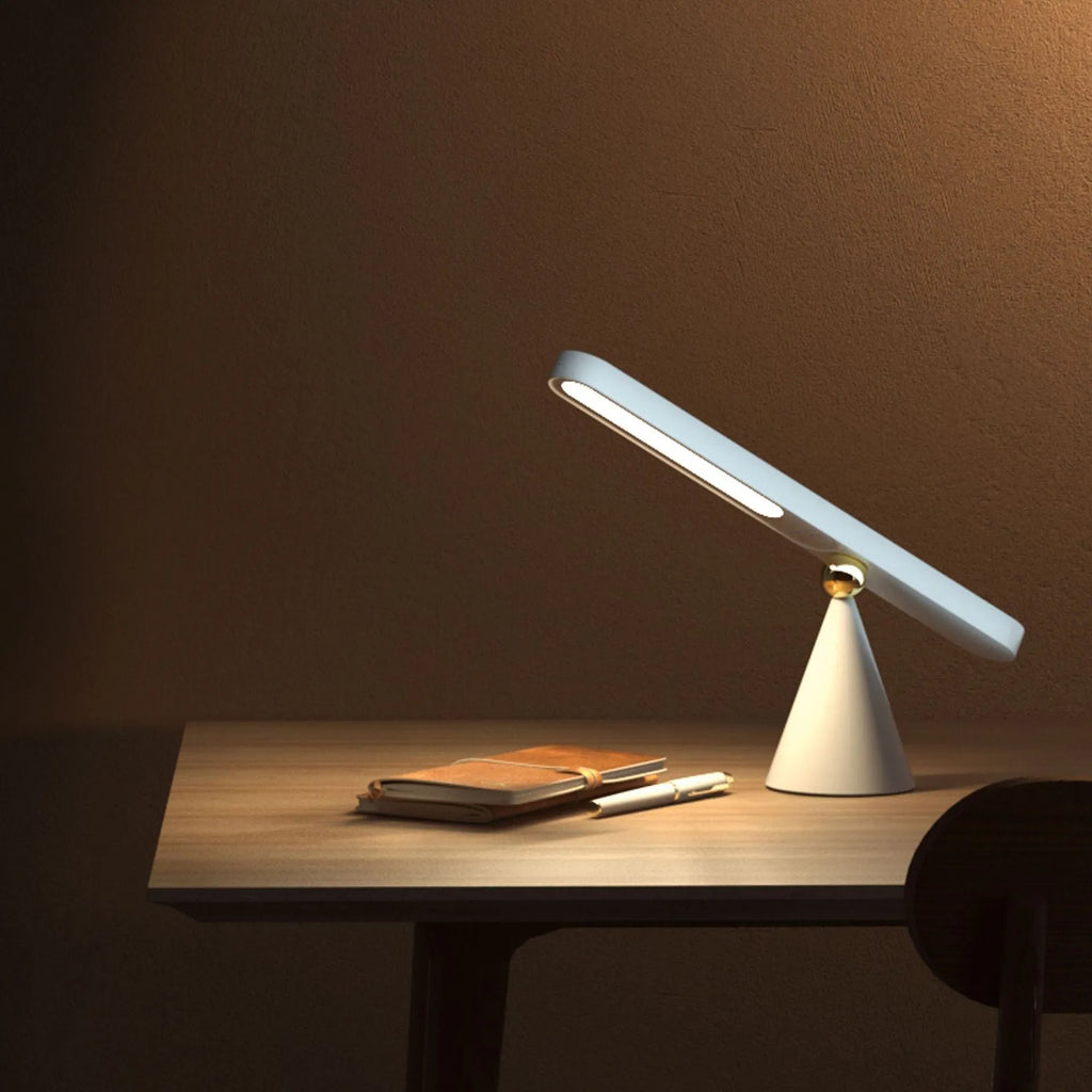White geometric desk lamp with touch control and magnetic base on a wooden table.