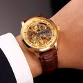Men's automatic mechanical watch with skeleton dial, leather strap, and gold-tone case on a neutral background