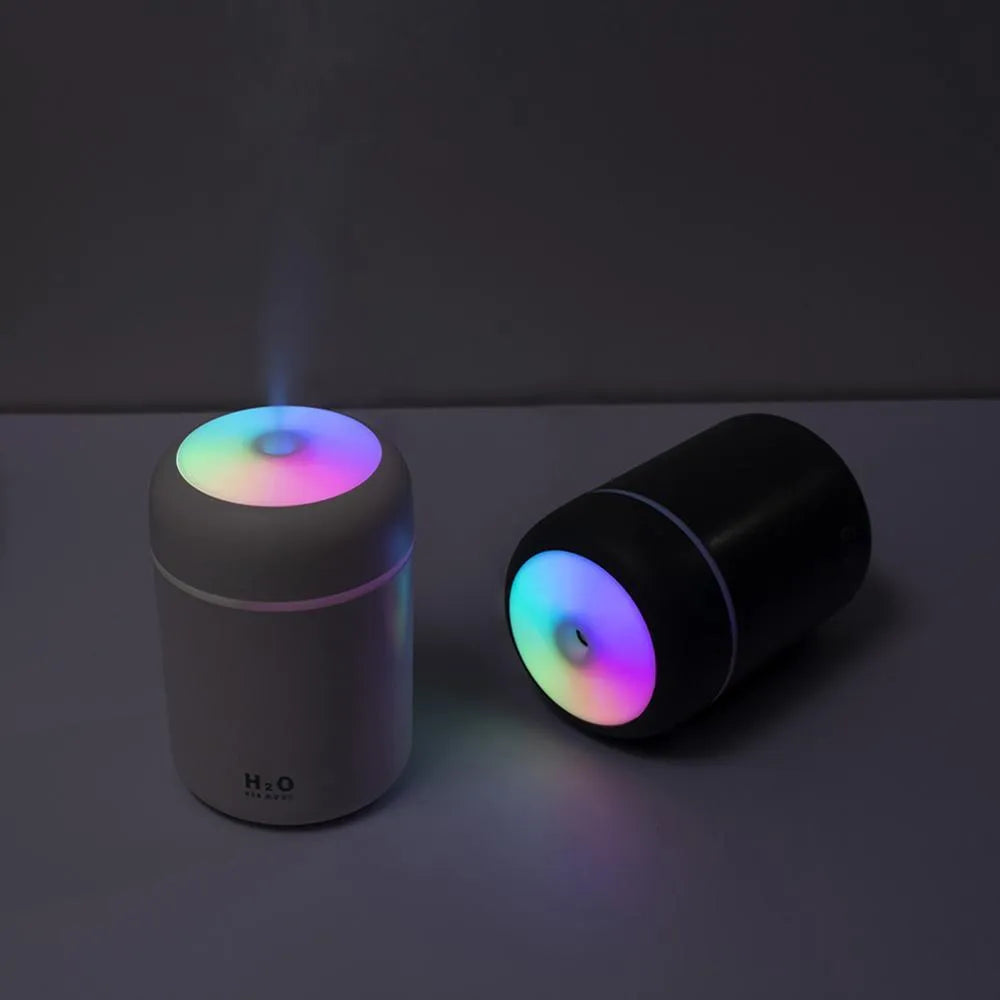 Pink USB mini humidifier with LED lights on wooden desk beside laptop