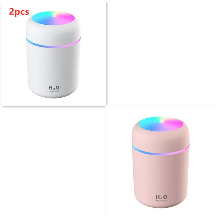 Pink USB mini humidifier with LED lights on wooden desk beside laptop