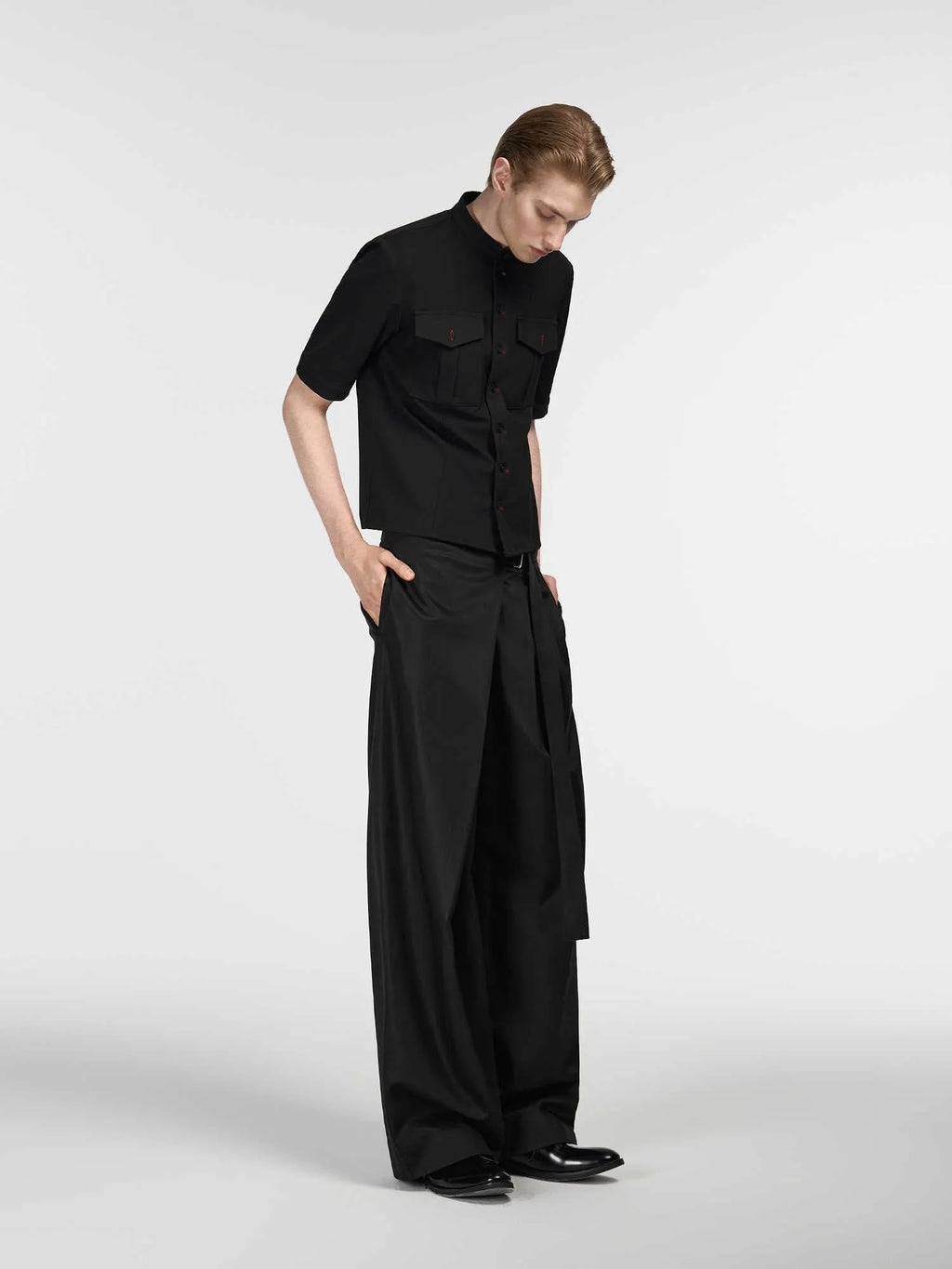 Black loose fit straight leg trousers with a single pleat and adjustable waistband on a hanger.