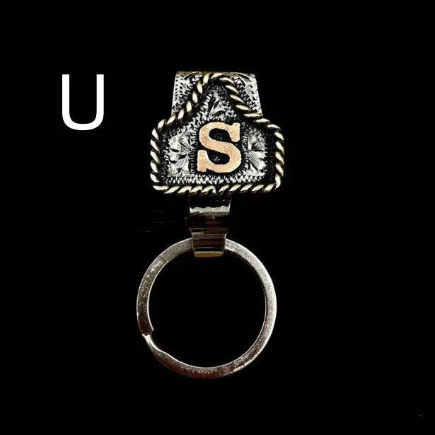 Handmade metal cow tag belt keychain showing one of 26 colour options, each marked with a different alphabet letter.