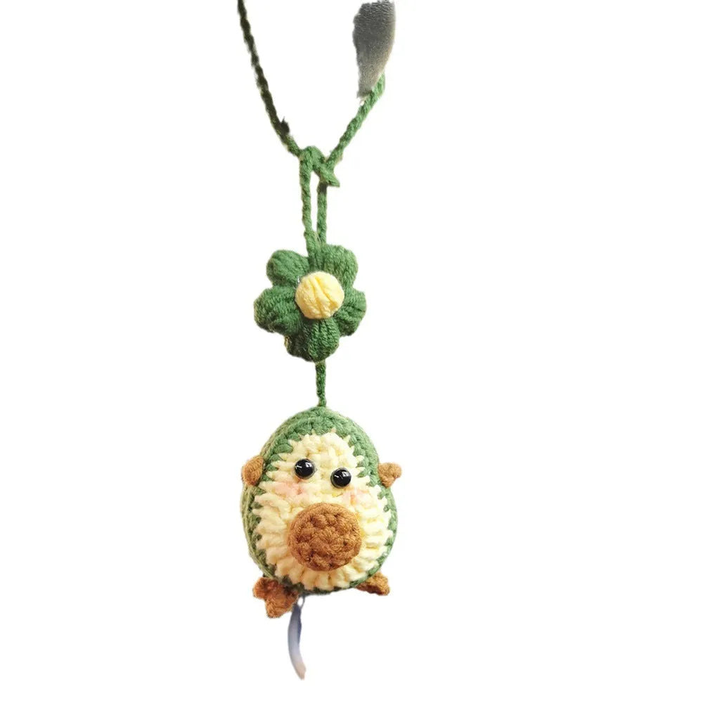 Handmade crocheted avocado-shaped car pendant with a rainbow flower on a green background.