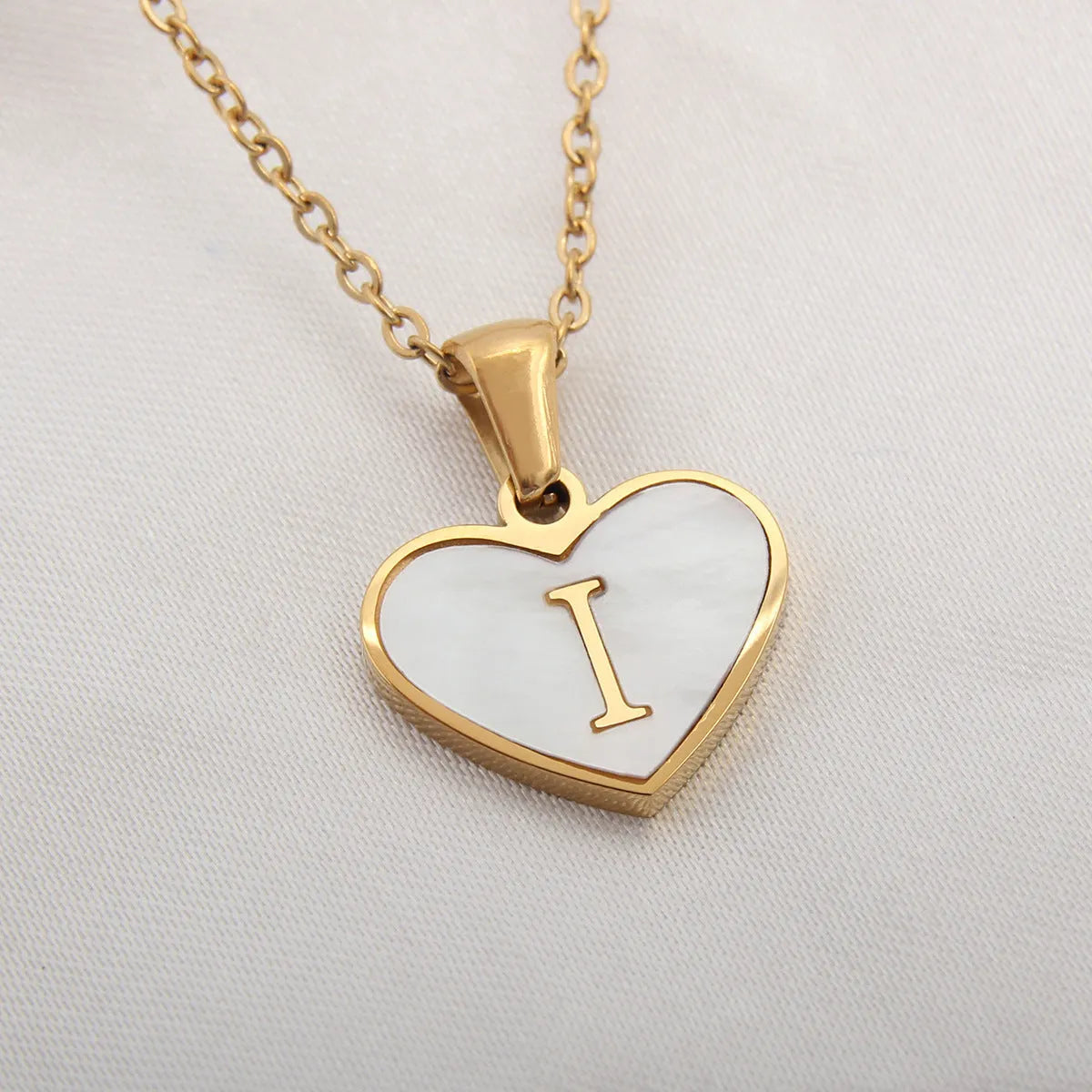 Gold-plated heart necklace with white shell pendant showing initial engraving on stainless steel chain
