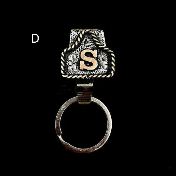 Handmade metal cow tag belt keychain showing one of 26 colour options, each marked with a different alphabet letter.