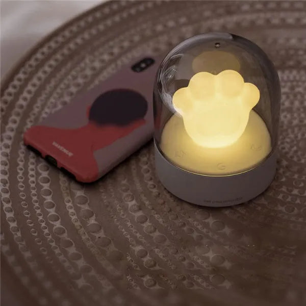 Grey cat paw shaped USB rechargeable night light with music box on a desk.