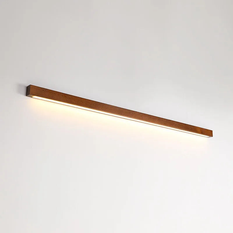 Modern walnut-coloured wood and acrylic log strip wall lamp in three lengths on a white wall.