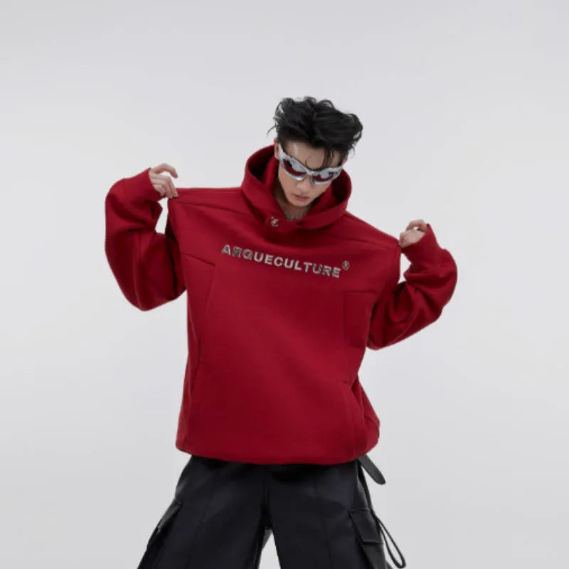Man wearing a loose black hooded sweater with metallic 3D printed design and structured shoulder pads.